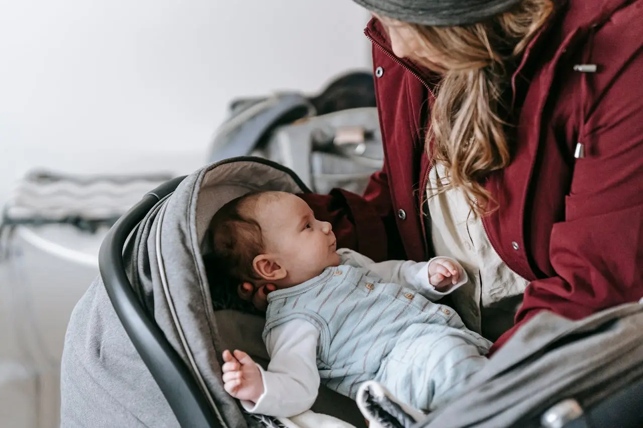 A baby in a striped sleeper looks up from a car seat, illustrating a stroller car seat system