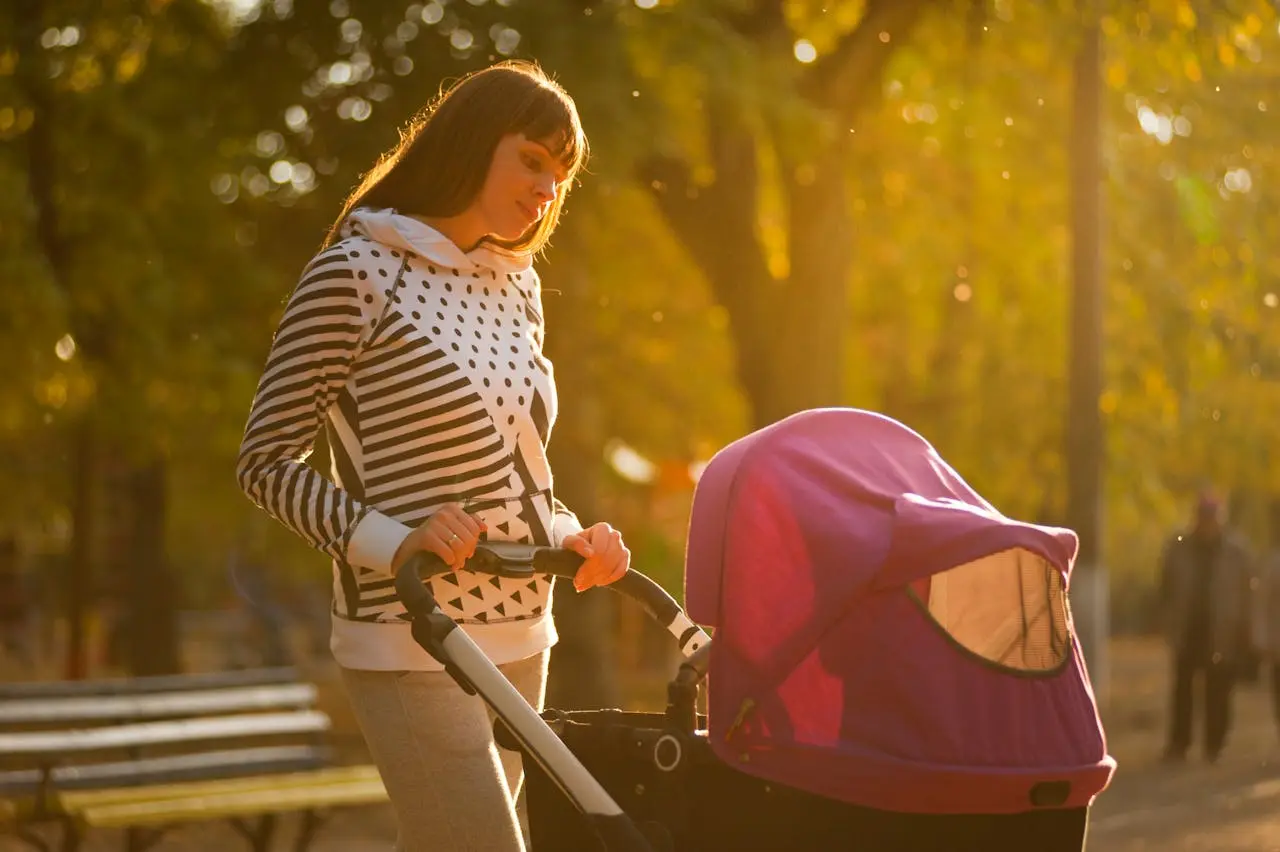 A woman in a striped hoodie pushes a baby stroller in a park, suitable for an article about umbrella strollers