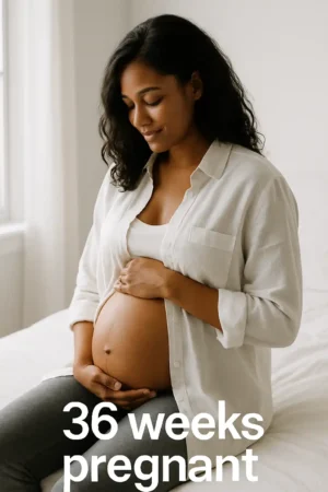 Seated pregnant person in a white button-down and tank top, hands supporting a bare belly with a faint linea nigra; soft window light; overlaid text reads “36 weeks pregnant.”