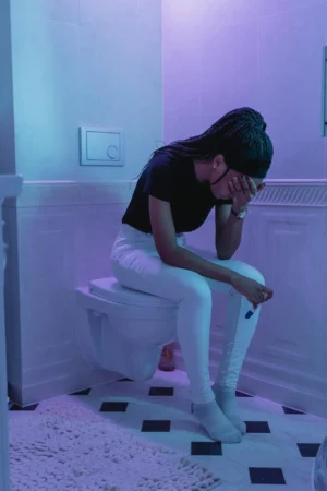 Person sitting on a toilet with head in hand, holding a test, illustrating discomfort from First Trimester Constipation.