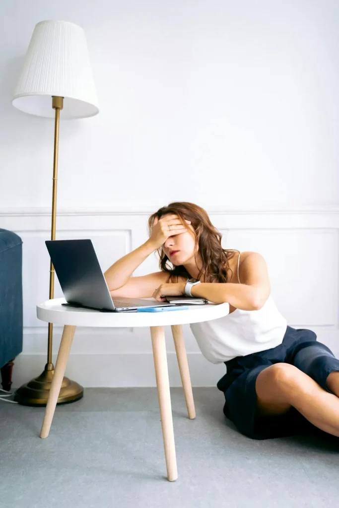 Tired pregnant woman sitting on the floor beside a small table and laptop, covering her eyes with one hand—illustrating pregnancy First Trimester Fatigue.
