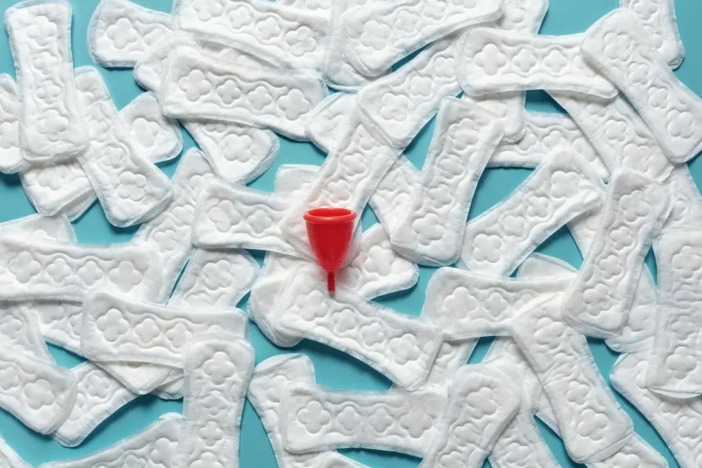 Flat-lay of scattered white panty liners with a red menstrual cup on a blue background, symbolizing First Trimester Increased Vaginal Discharge and everyday management.