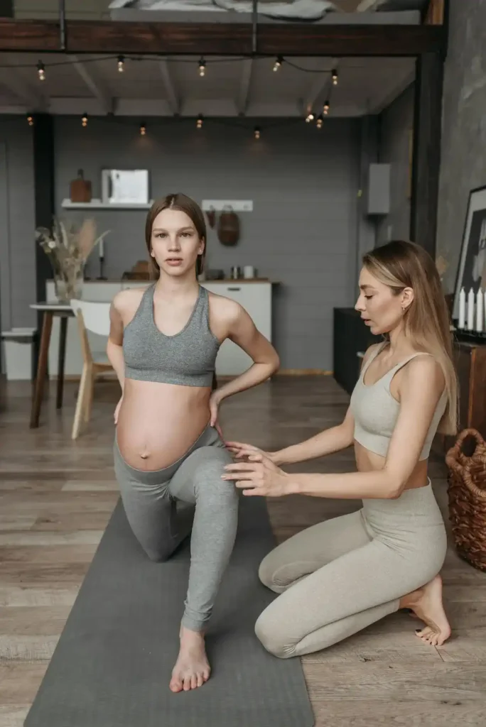 Pregnant woman practicing a supported lunge with a trainer—joint-friendly, low-impact aerobics for pregnancy on a yoga mat in a calm home studio.