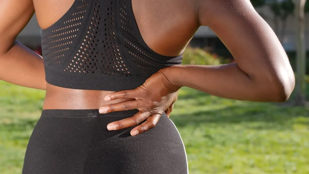 Close-up of a person outdoors holding their lower back, illustrating Backaches and Round Ligament Pain during pregnancy.