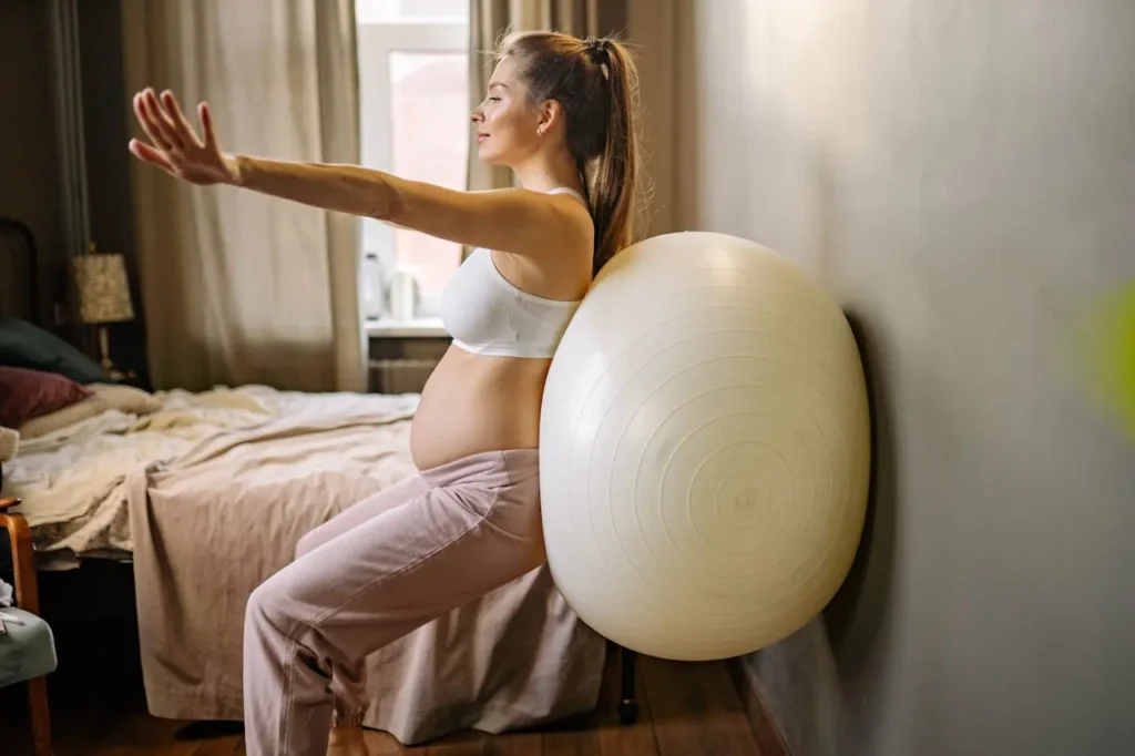 Pregnant woman doing a wall squat with an exercise ball at home, showing The Benefits of Exercising During Pregnancy.