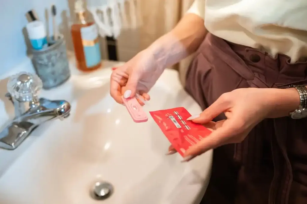 Close-up of a woman in a bathroom holding an ovulation/pregnancy test and its wrapper over a sink—a moment paired with learning the best diet for getting pregnant.