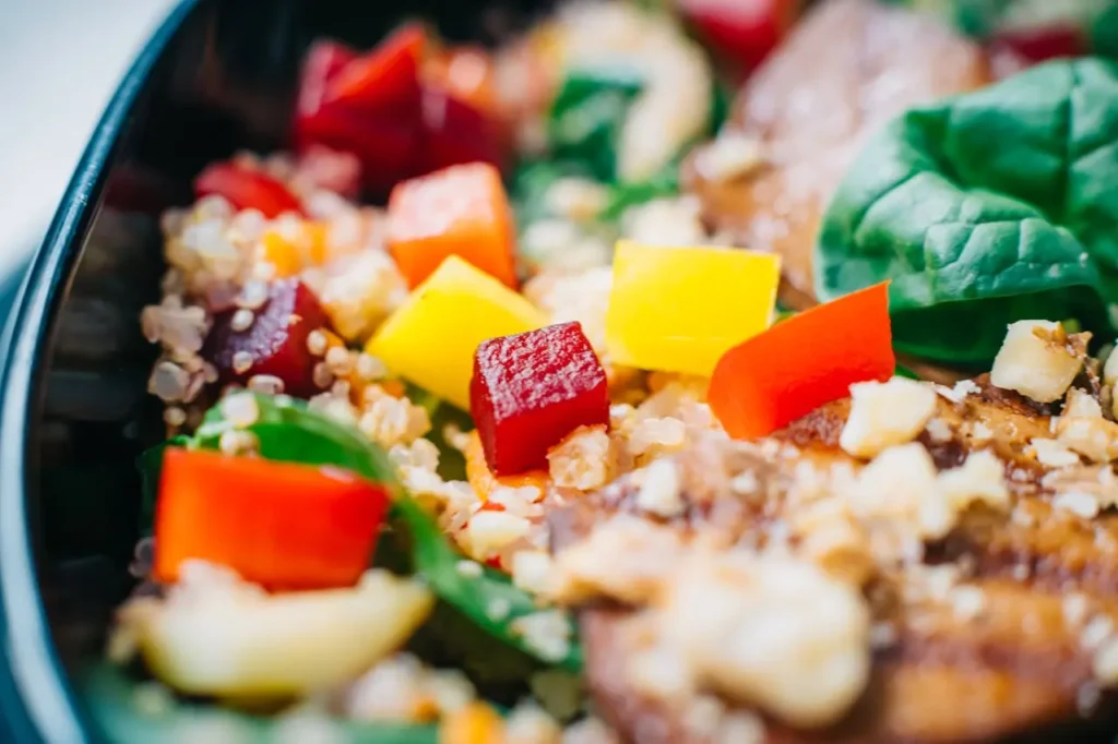 Close-up of a nourishing Dinner for Pregnancy bowl with quinoa, diced red and yellow veggies, beet cubes, fresh spinach leaves, and crunchy nut topping.