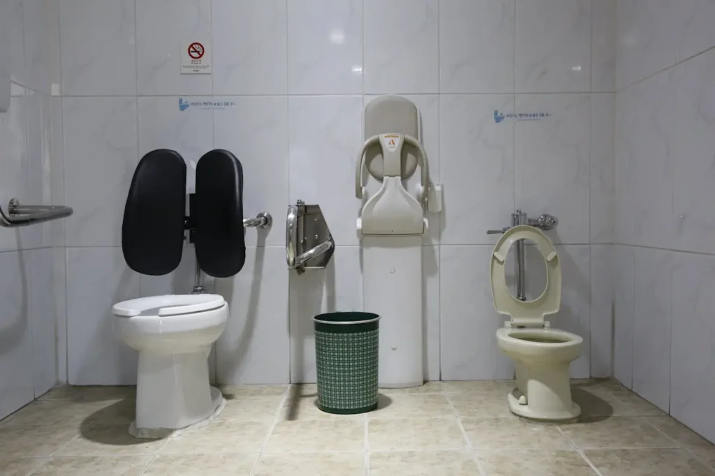 Accessible tiled restroom with an adult toilet, child-size toilet, grab bars, wall-mounted changing table, and a green waste bin—illustrating First Trimester Frequent Urination and frequent bathroom trips.