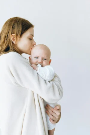 New mom in a cozy robe kisses her baby while holding them close—calm moment symbolizing healthy eating for postpartum recovery and gentle self-care.