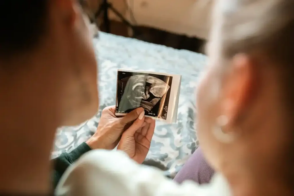 Couple sitting on a bed, tenderly holding an ultrasound photo—reflecting on how long it takes to get pregnant naturally.