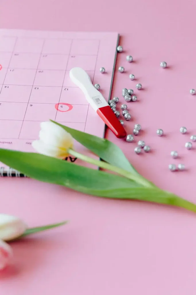 Positive pregnancy test on a pink calendar with ovulation dates circled, tulips and confetti nearby—visual for how to get pregnant fast planning.