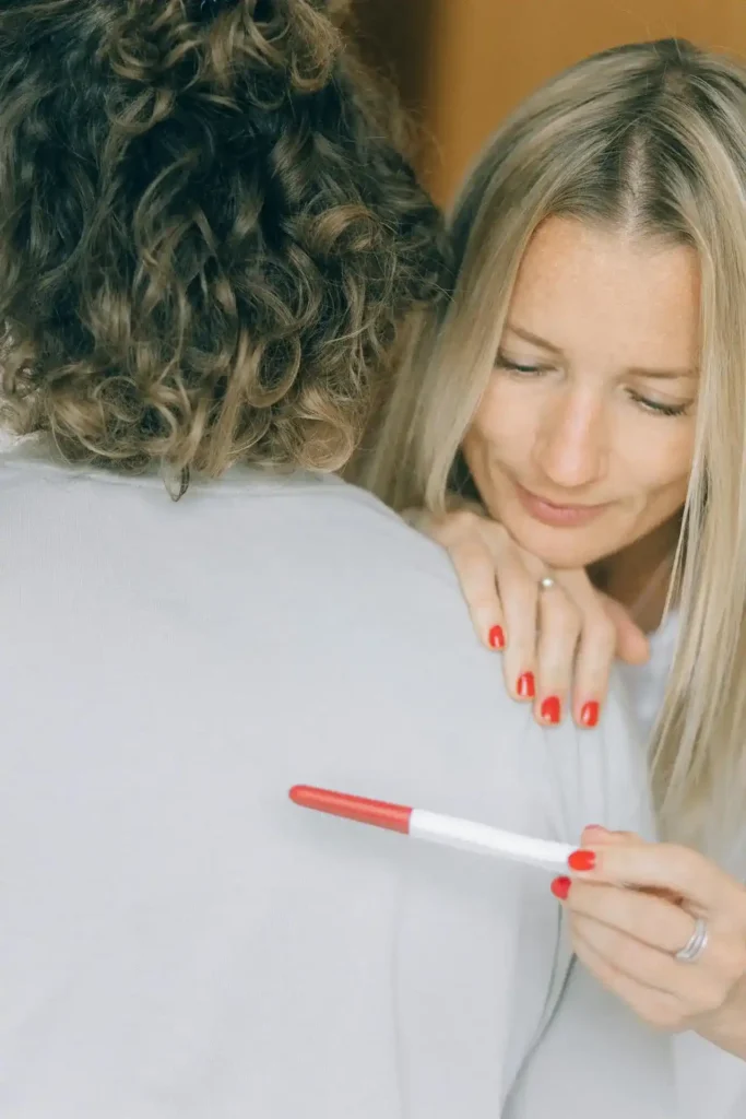 Woman hugging her partner while holding a pregnancy test—tender moment that hints at planning and preparing the body for pregnancy.