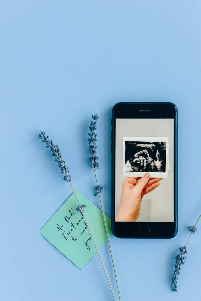 Flat-lay of a smartphone with a hand holding an ultrasound photo on the screen, lavender sprigs, and a small note—visual guide for how to track ovulation.
