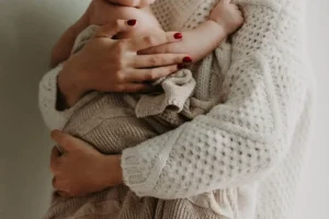 Close-up of a new mom in a cream knit sweater cradling her swaddled baby—calm, supportive moment during postpartum Pelvic floor issues recovery.