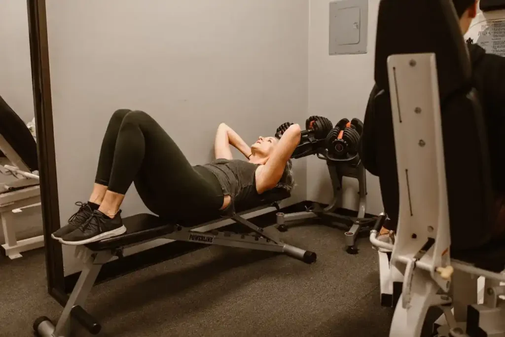 Woman performing a core move on an incline bench at the gym—example of postpartum specific exercises done with control and proper form.