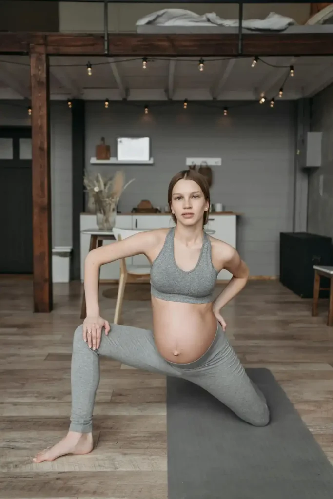 Pregnant woman practicing a supported side-lunge stretch on a yoga mat at home, following Safety Guidelines for Pregnancy Exercise.