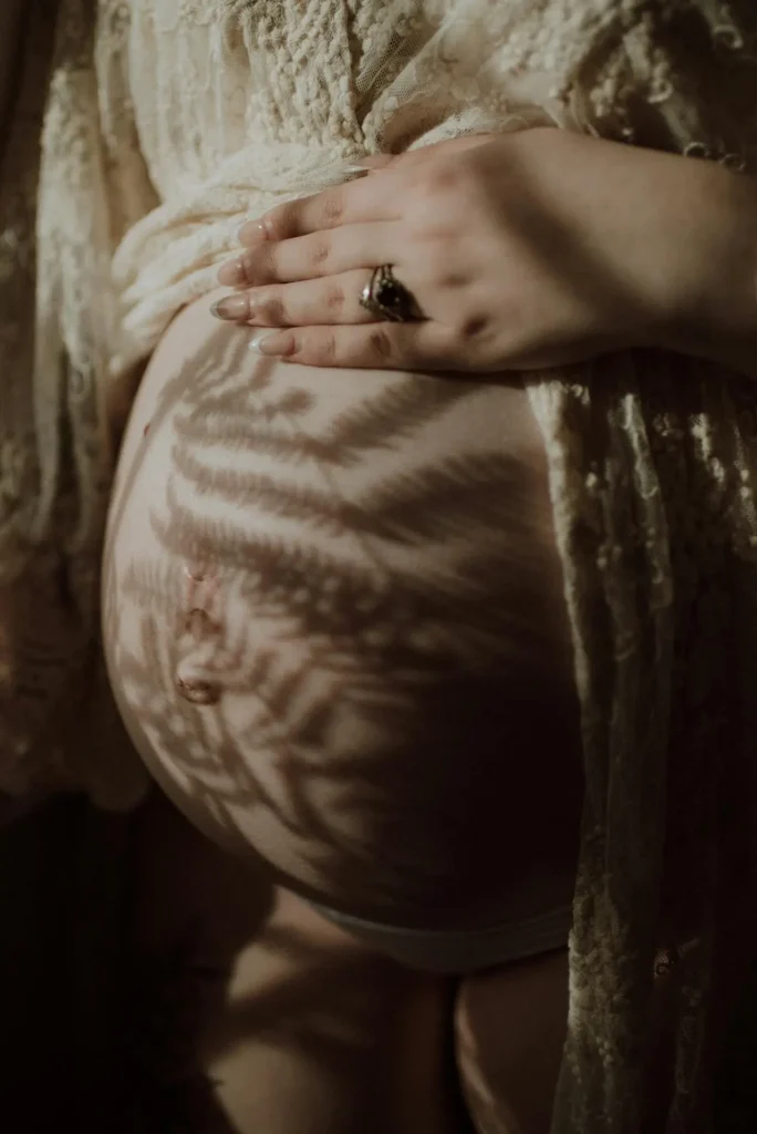 Close-up of a pregnant belly with a hand resting on it and lace shadows—visual for Second Trimester Braxton Hicks Contractions (“practice” tightenings).
