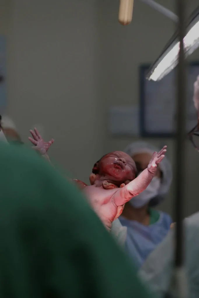 Newborn lifted by a clinician in a hospital delivery room—arms outstretched moments after birth—illustrating the final stage in the stages of labor.