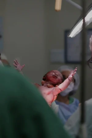 Newborn lifted by a clinician in a hospital delivery room—arms outstretched moments after birth—illustrating the final stage in the stages of labor.