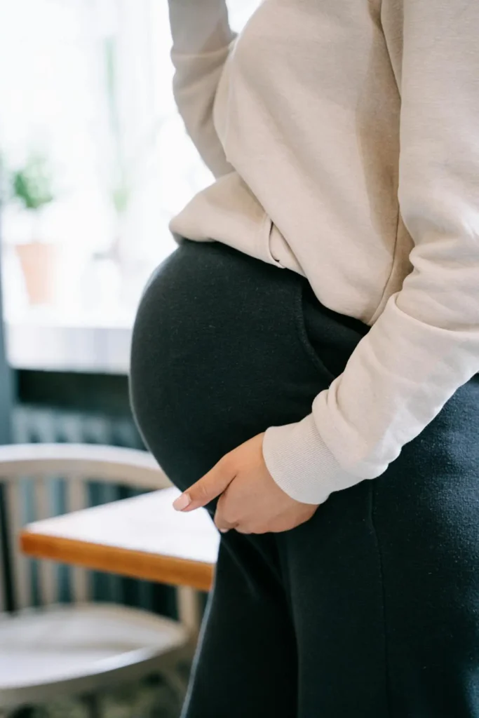 Pregnant woman in a cozy sweatshirt holding her bump, illustrating third trimester symptoms like pelvic pressure, backache, and Braxton Hicks.