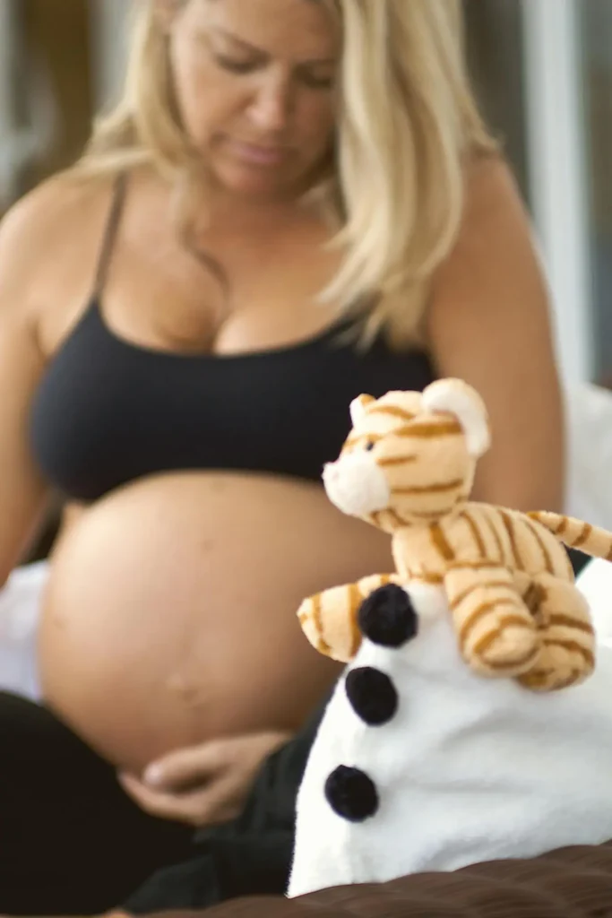 Pregnant woman resting a hand on her belly beside a small tiger plush—gentle reminder of tips for dealing with anxiety about childbirth.
