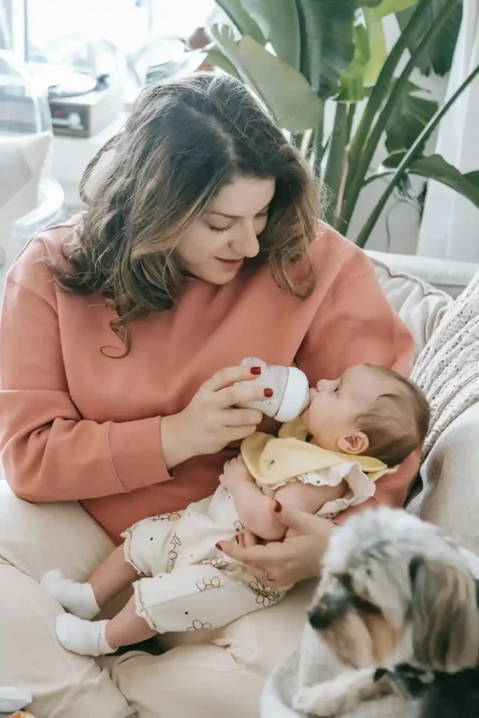 Mom sitting on a cozy couch and bottle-feeding her infant while a small dog rests nearby, illustrating baby Combo Feeding in a relaxed home setting.