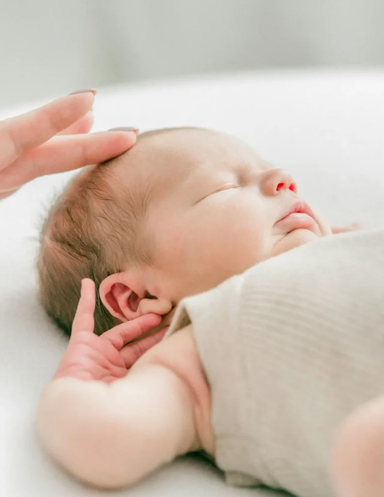 Parent gently touching a sleeping baby’s forehead, checking for warmth as part of a baby fever guide.