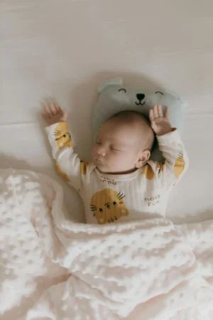 Baby sleeping on their back with arms up, tucked under a soft blanket, illustrating Baby Sleep by Age : 0–12 Months.