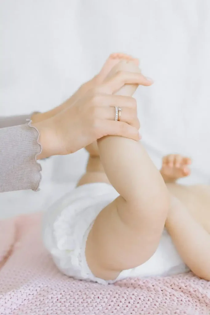 Mother gently lifting her baby’s legs during a diaper change, demonstrating proper diapering newborn hygiene.