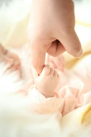 Close-up of a newborn gently gripping an adult’s finger during the first week home with baby, with soft pastel blankets in the background.