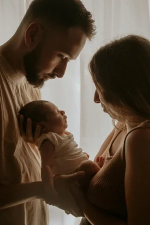 Young parents gently holding and comforting their newborn in soft light, illustrating how to soothe a fussy or colicky newborn with closeness and calm.