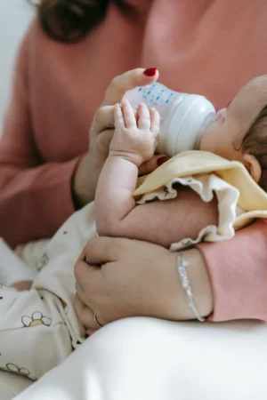 Parent holding a young baby while offering a bottle, illustrating a calm moment that fits into a newborn feeding schedule by age (0–6 months).