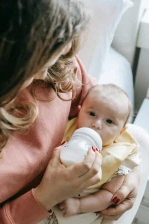 Mom holding her baby in her arms and offering a bottle of expressed milk, illustrating pumping and breast milk storage basics for new moms.