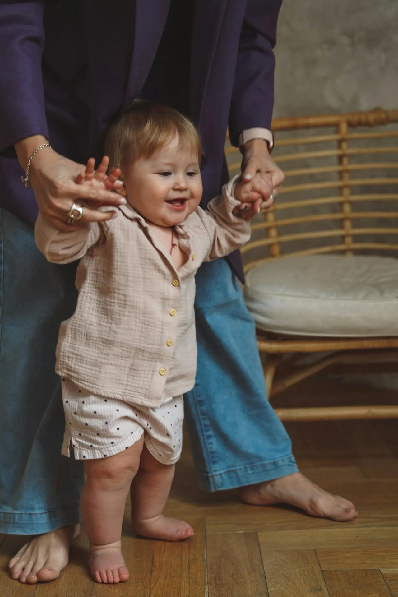 Smiling baby taking supported steps while an adult holds their hands, showing typical progress and setting the scene for discussing red flags in baby development.
