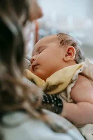 Close-up of a newborn sleeping on a caregiver’s chest, showing a peaceful contact nap while talking about safe sleep guidelines to reduce SIDS risk.