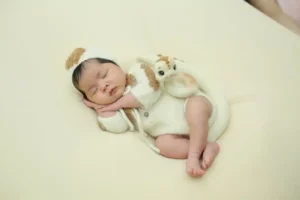 Newborn sleeping on a cream backdrop in a knit outfit with a tiny plush prop—Sleep Habits for Baby visual.