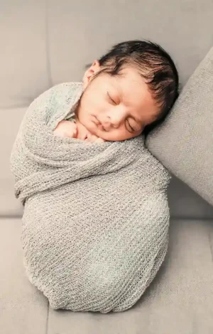 Swaddling baby wrapped snugly in a soft neutral knit blanket, sleeping peacefully on a cushioned surface.