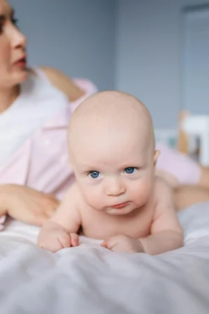 Newborn baby practicing tummy time, lifting their head on a soft bed while a parent watches nearby, showing how tummy time for newborns builds strength.